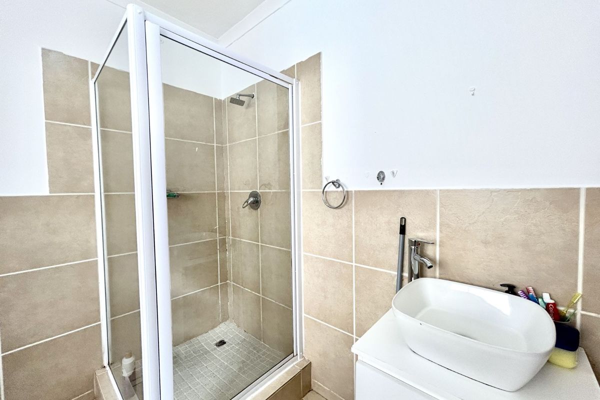 A functional bathroom featuring a glass-enclosed shower with beige tiling and a modern vessel sink vanity unit.