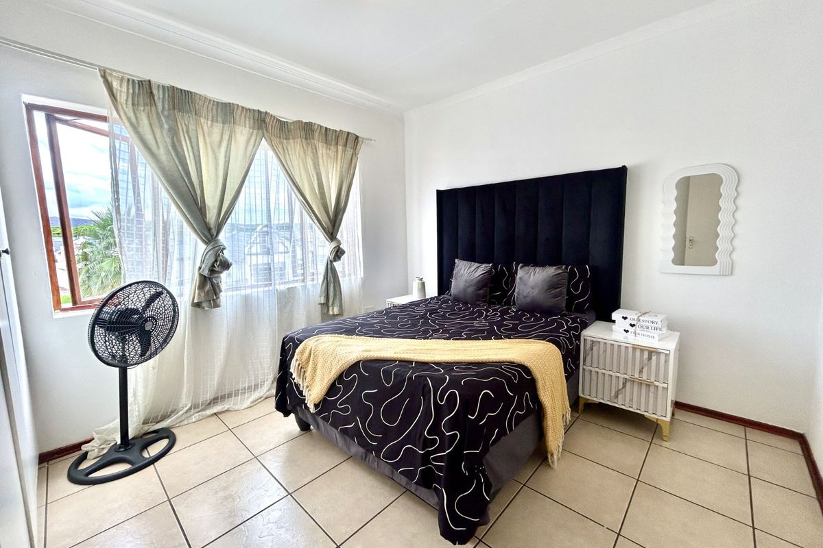 A bright bedroom featuring tiled flooring, a large window with curtain treatments, and a ceiling-mounted light fixture.