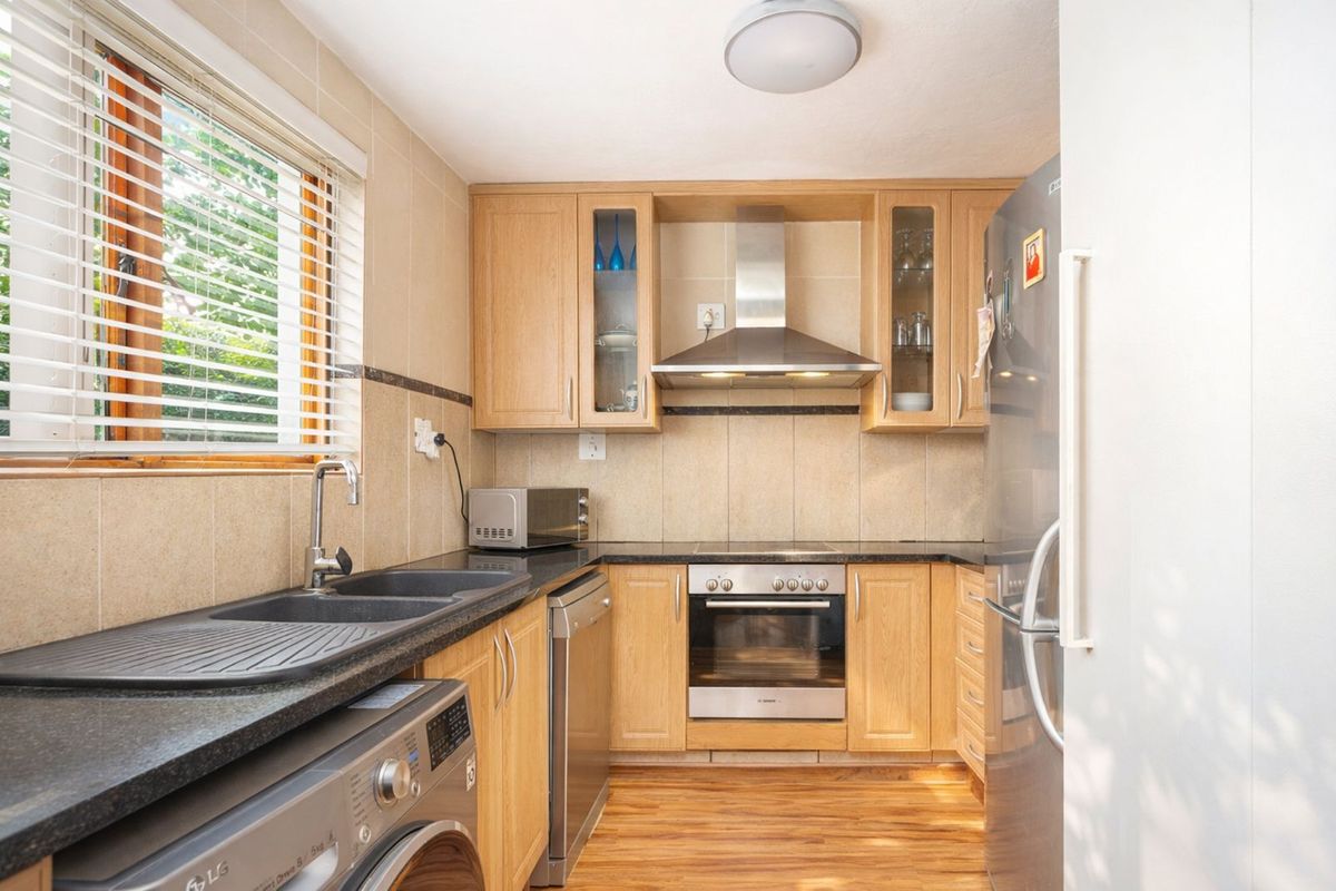 A functional kitchen featuring light wood cabinetry, dark granite countertops, a built-in oven, extractor fan, and integrated sink with tiled splashbacks.