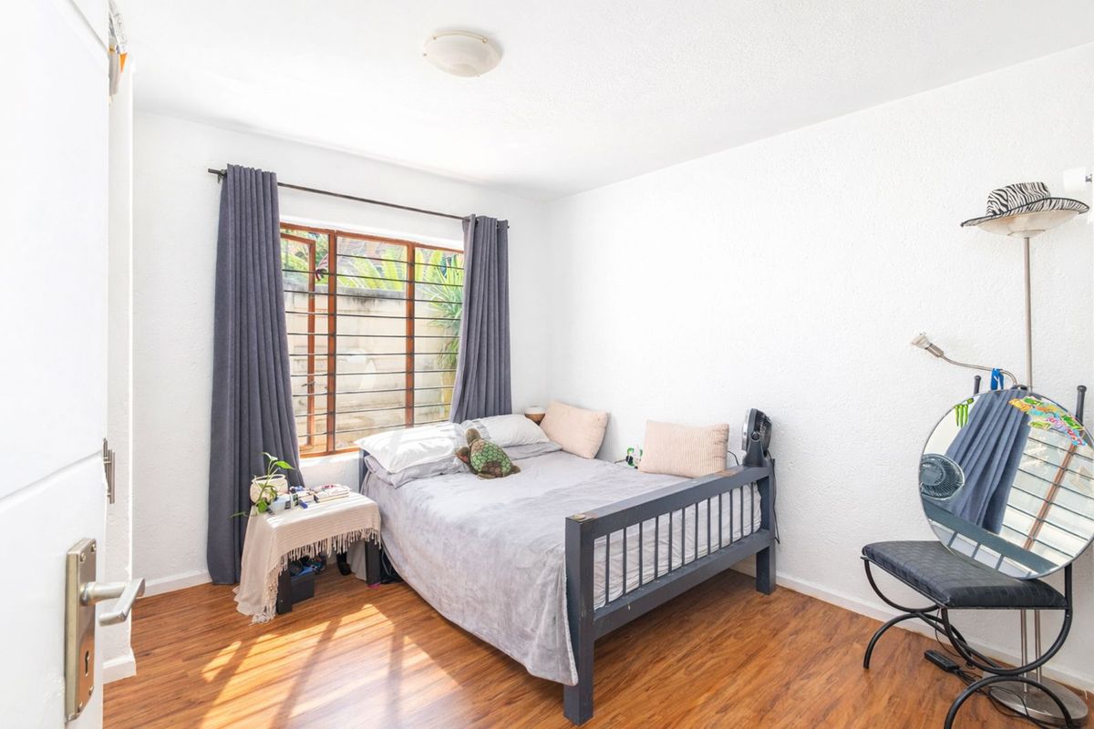 A bright bedroom featuring wood-look laminate flooring, a window with security bars, and a flush-mount ceiling light fixture.