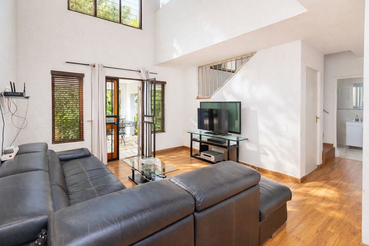 Spacious double-volume living area featuring laminate flooring, large windows, and direct access to an outdoor patio space.