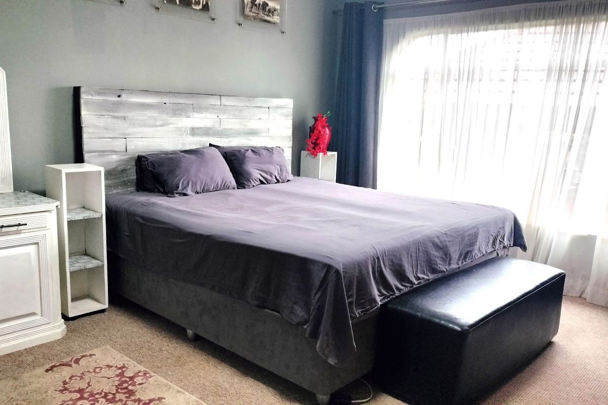 A bedroom featuring carpeted flooring, neutral wall tones, and large windows with curtains allowing natural light.