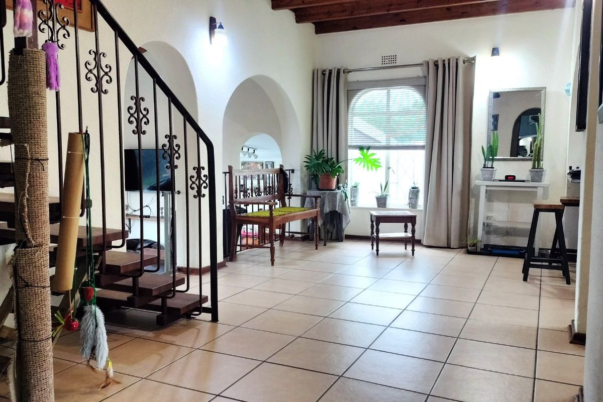 Spacious living area featuring tiled flooring, arched architectural details, exposed timber ceiling beams, and a wrought iron staircase.