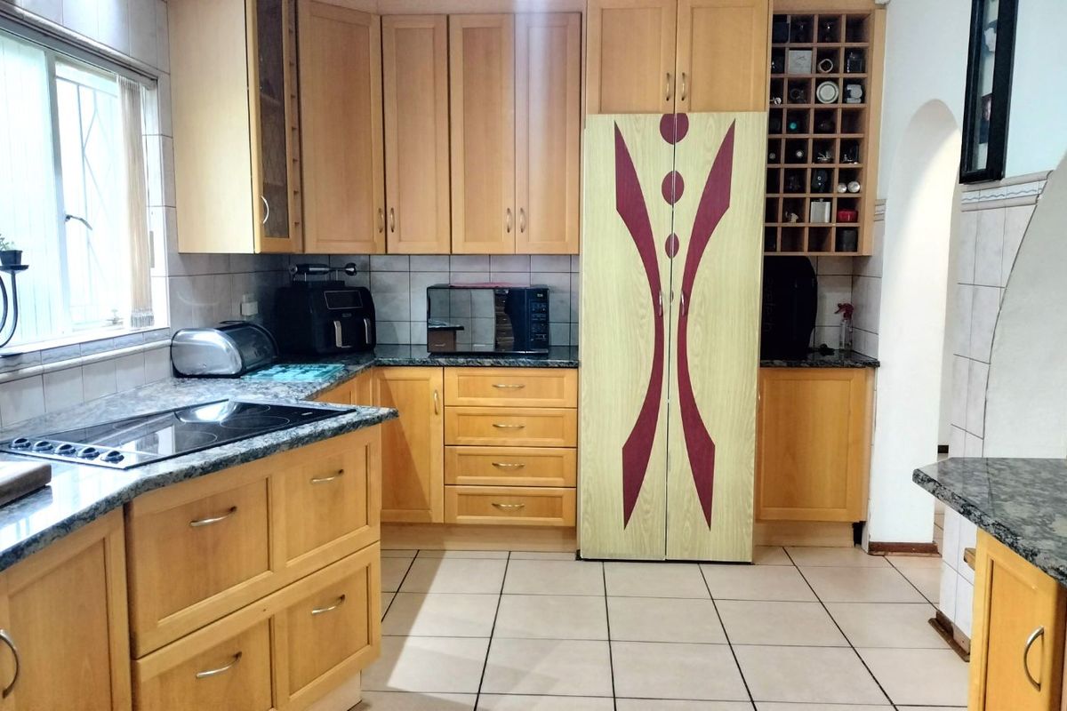 A functional kitchen featuring light wood cabinetry, granite countertops, a built-in hob, and tiled flooring with a dedicated wine rack storage area.
