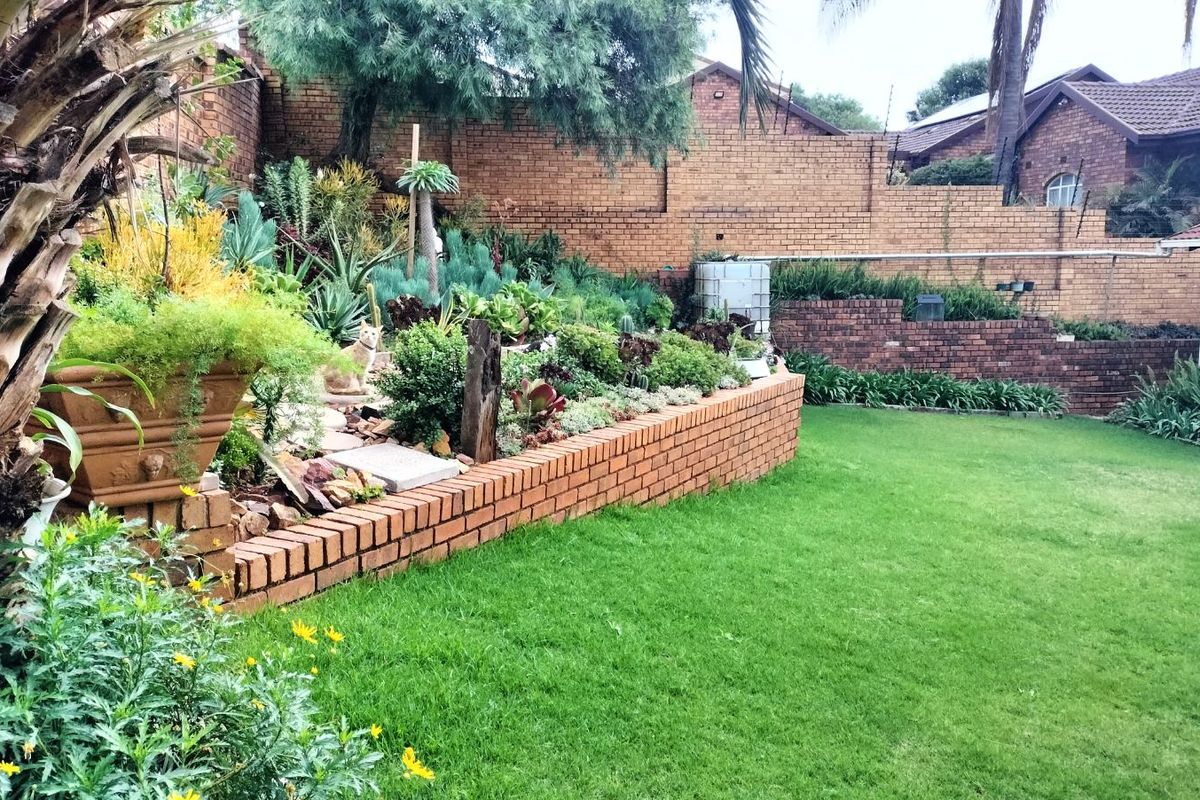 A well-maintained rear garden featuring tiered brick retaining walls, established landscaping, and a lush green lawn.