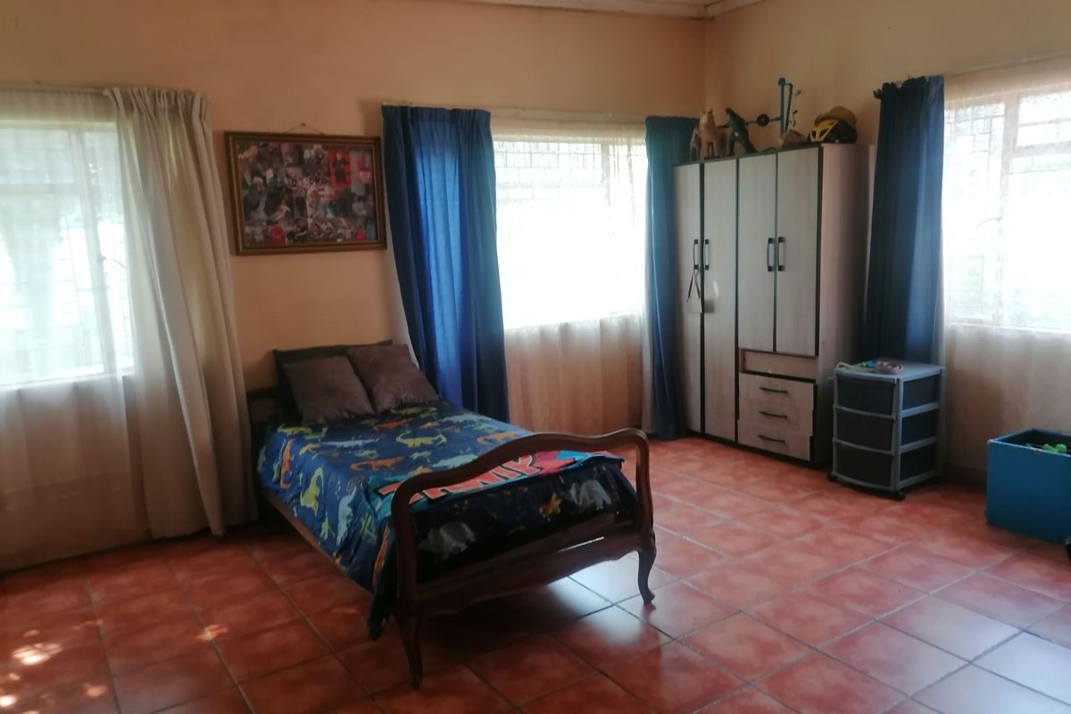 A spacious bedroom featuring terracotta floor tiles, large windows with natural light, and neutral wall tones, offering a functional layout for a bedroom space.