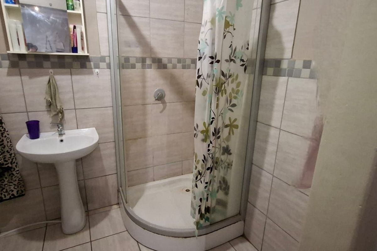 A functional bathroom featuring a corner shower enclosure with a glass door, a pedestal basin, and tiled walls with a decorative border.