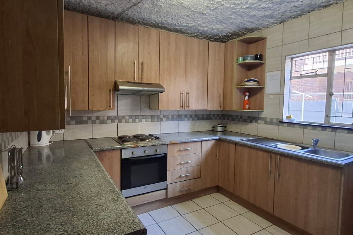 Functional kitchen featuring wood-look cabinetry, granite-style countertops, built-in oven, hob, extractor fan, and tiled splashbacks.