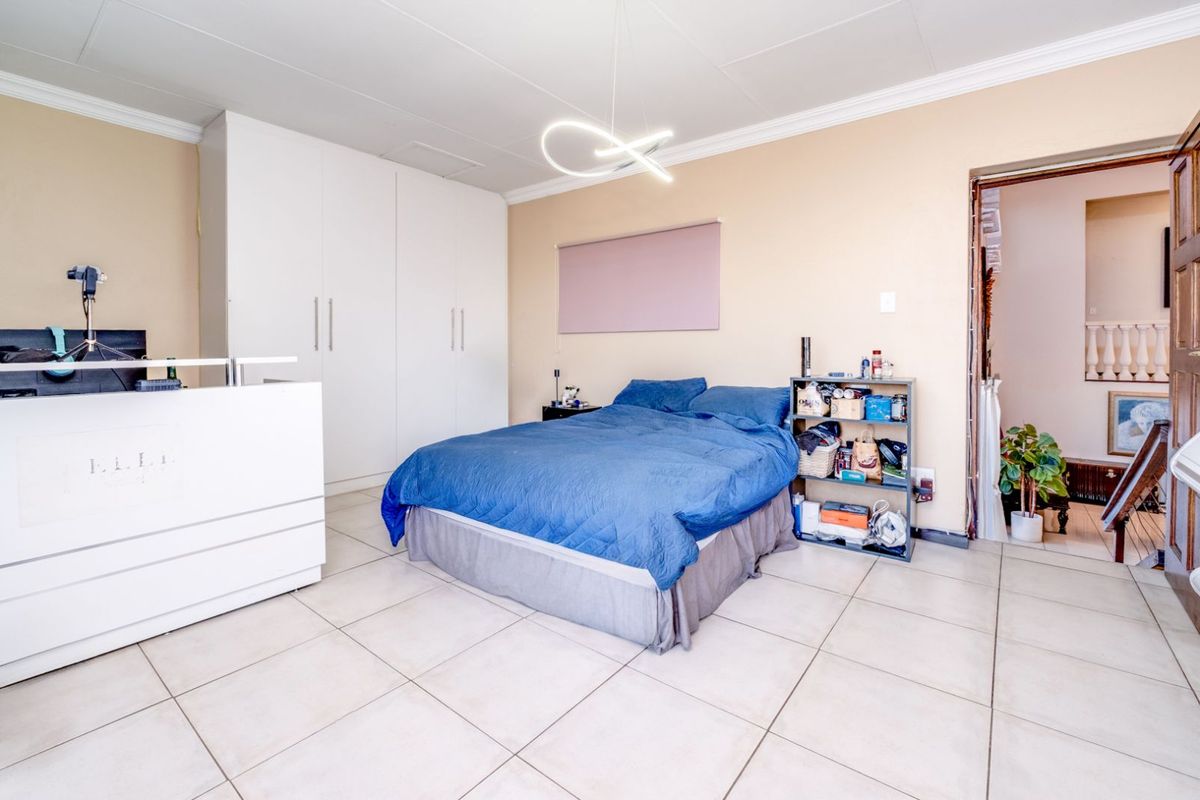 A spacious bedroom featuring large built-in wardrobes, tiled flooring, and a modern light fixture, with an adjacent room visible through the doorway.