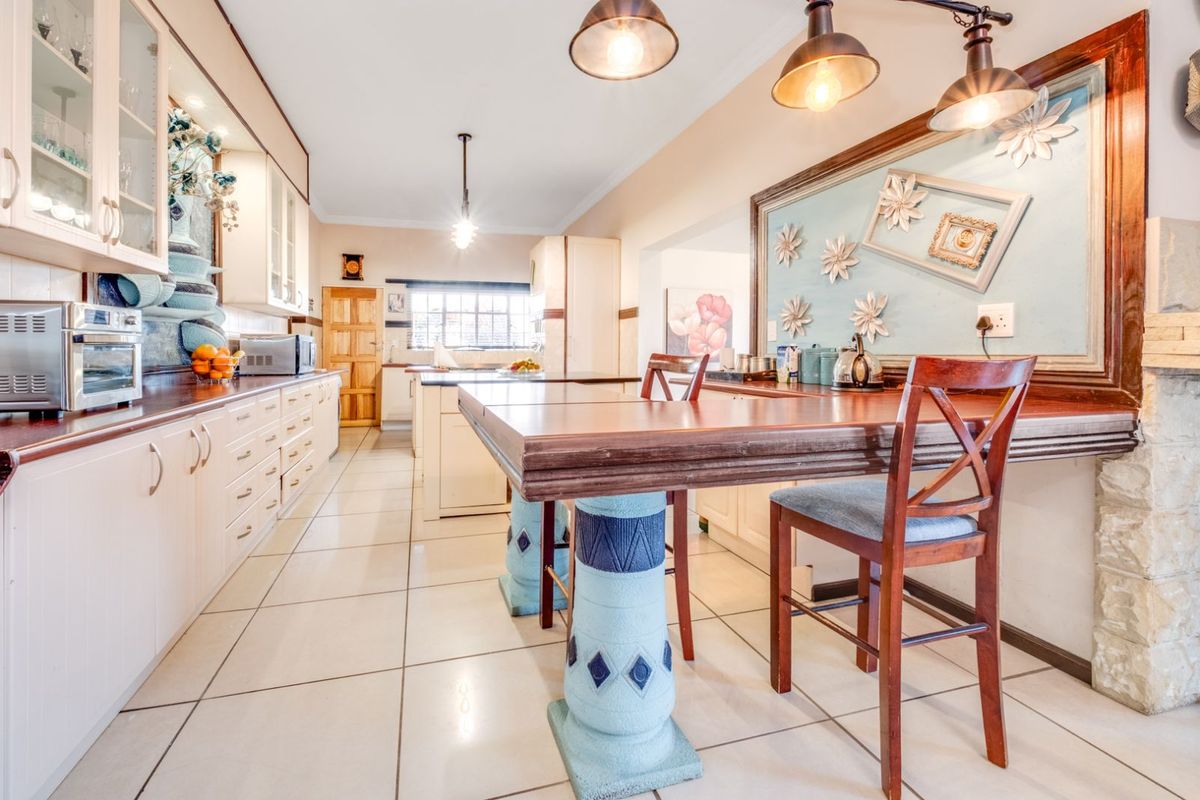 Spacious kitchen featuring extensive cabinetry, tiled flooring, and a built-in breakfast bar area with decorative pillars, offering a functional layout for daily use.