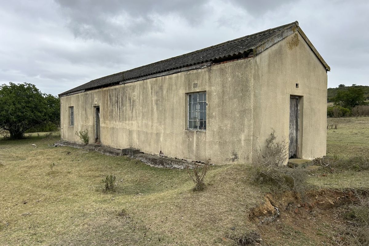 A detached farm building featuring a pitched roof and weathered exterior walls, situated on open rural land, requiring significant restoration and maintenance.