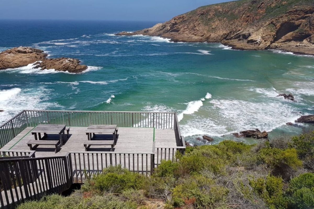 A scenic wooden viewing deck overlooking a coastal bay with rocky cliffs and ocean views.