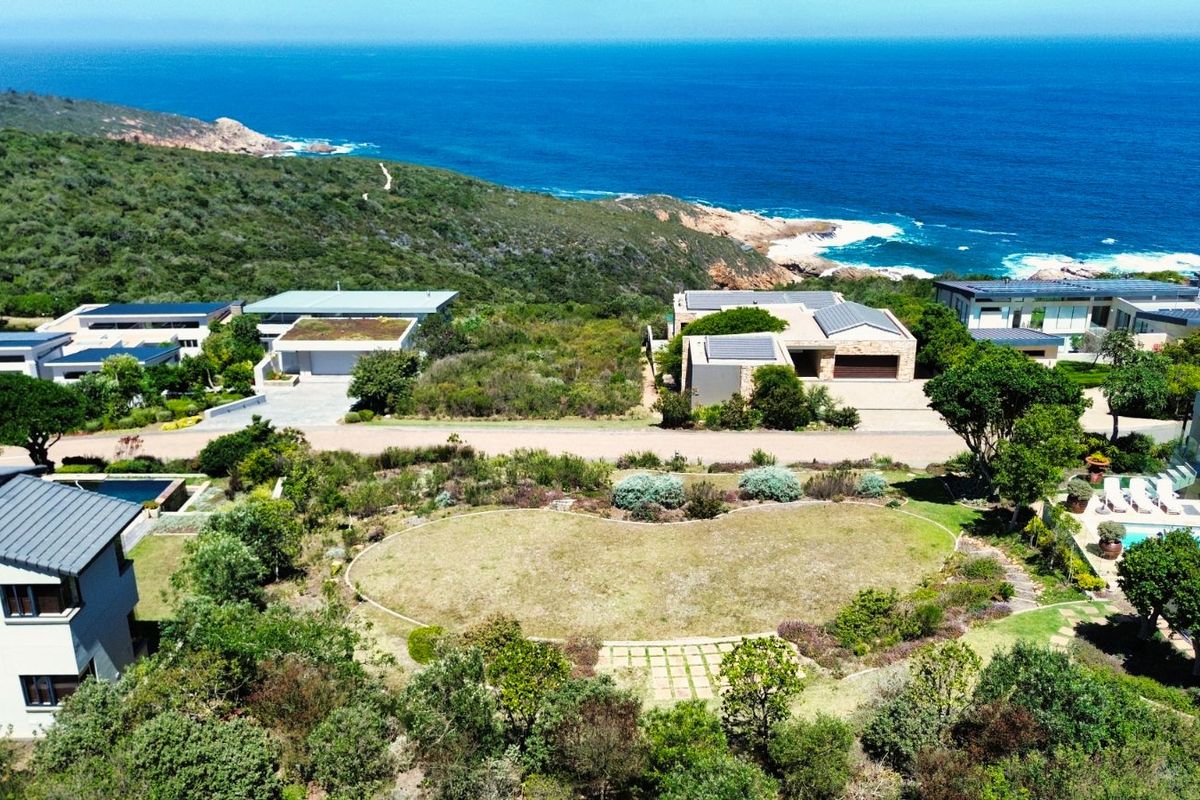 An elevated aerial view of a vacant residential plot situated in a coastal estate, surrounded by established luxury homes and natural vegetation.