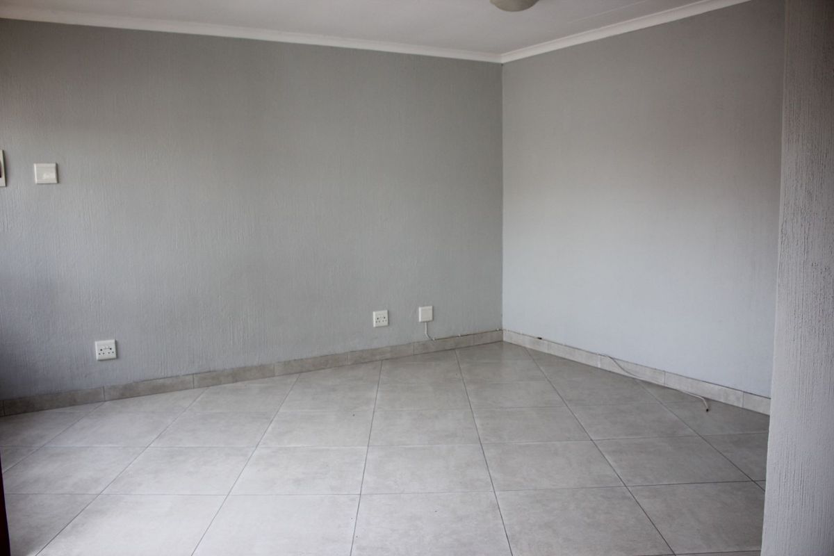 An empty, neutral-toned living area featuring tiled flooring, coved ceilings, and multiple electrical power points.