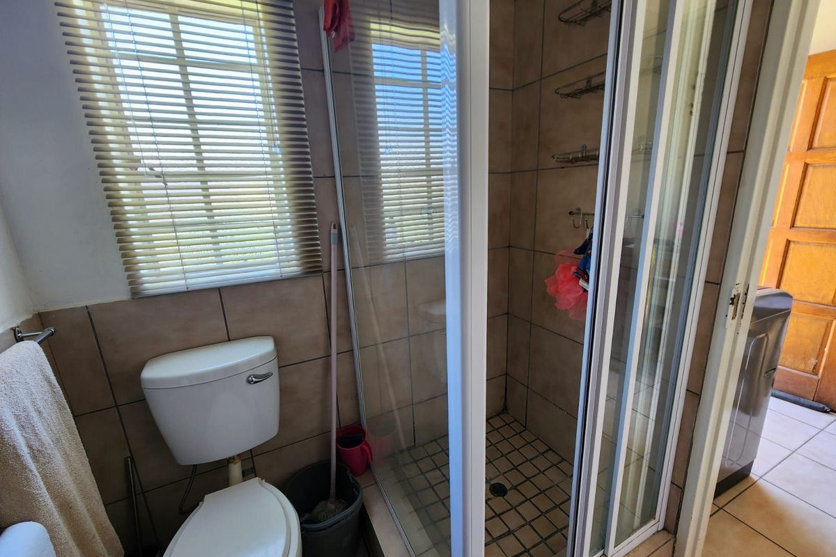 A functional bathroom featuring a glass-enclosed shower, ceramic wall tiling, and a standard toilet with a window for natural light.