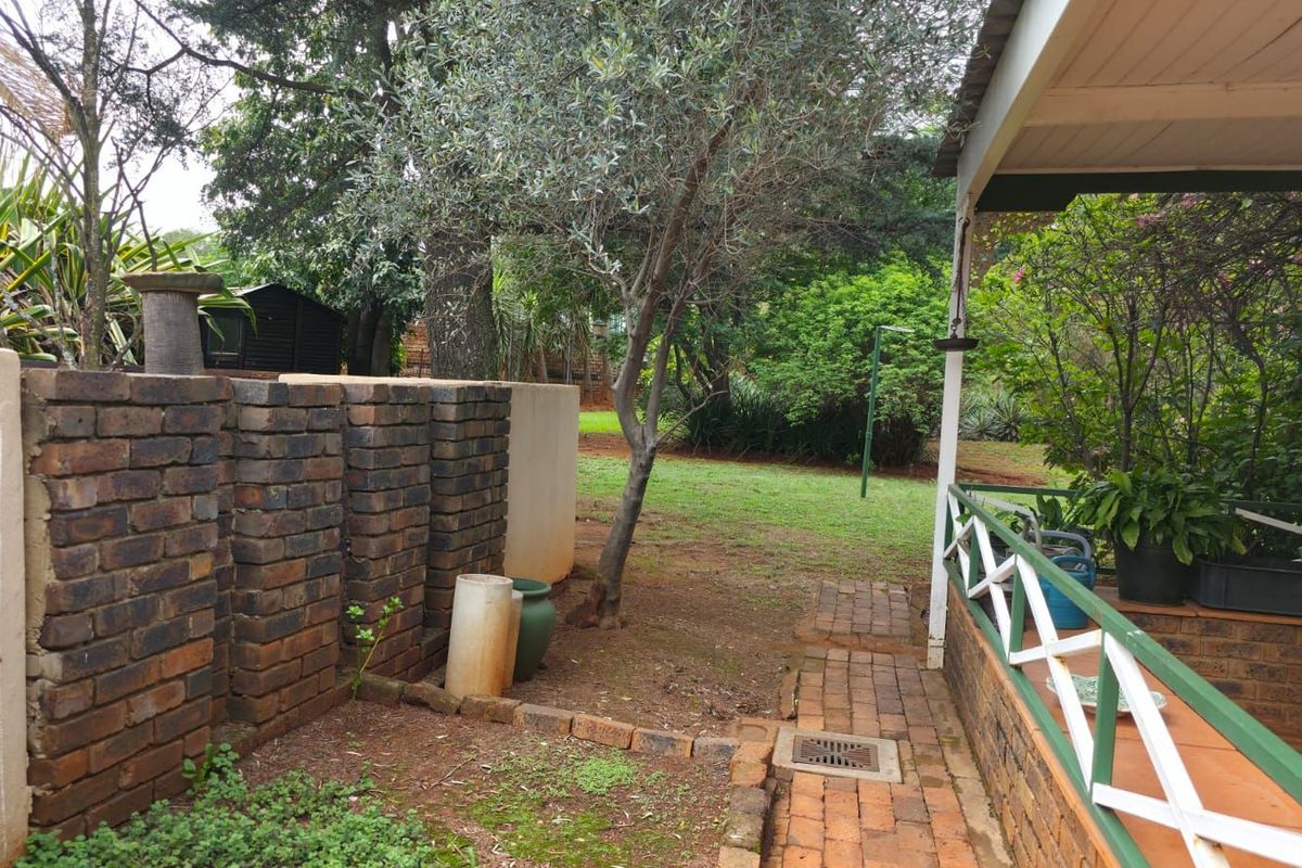 A view of the rear garden featuring a covered patio area, brick retaining wall, and established trees in a private backyard setting.