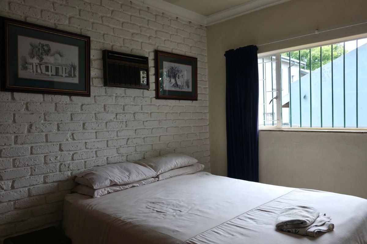 A bedroom featuring a white painted brick feature wall, built-in air conditioning unit, and a window with security bars.