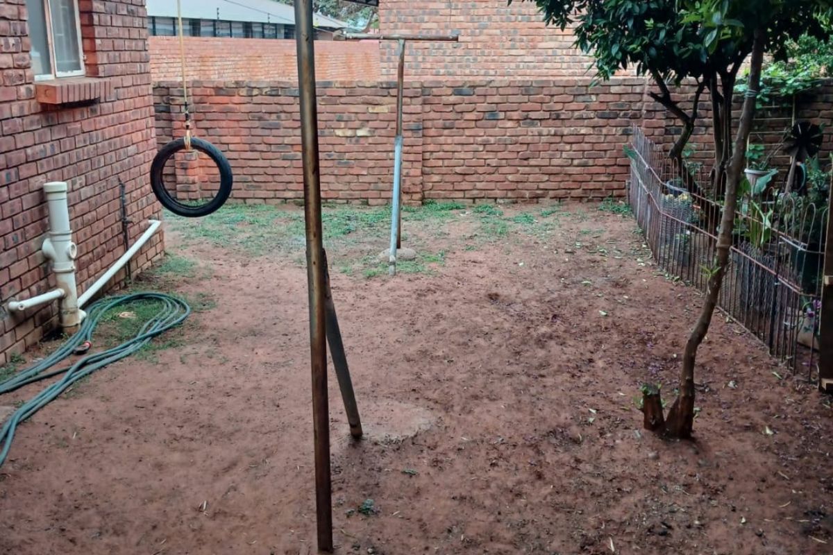 A rear garden area featuring exposed brick walls, a metal washing line structure, and a mature tree, offering potential for landscaping and outdoor improvement.