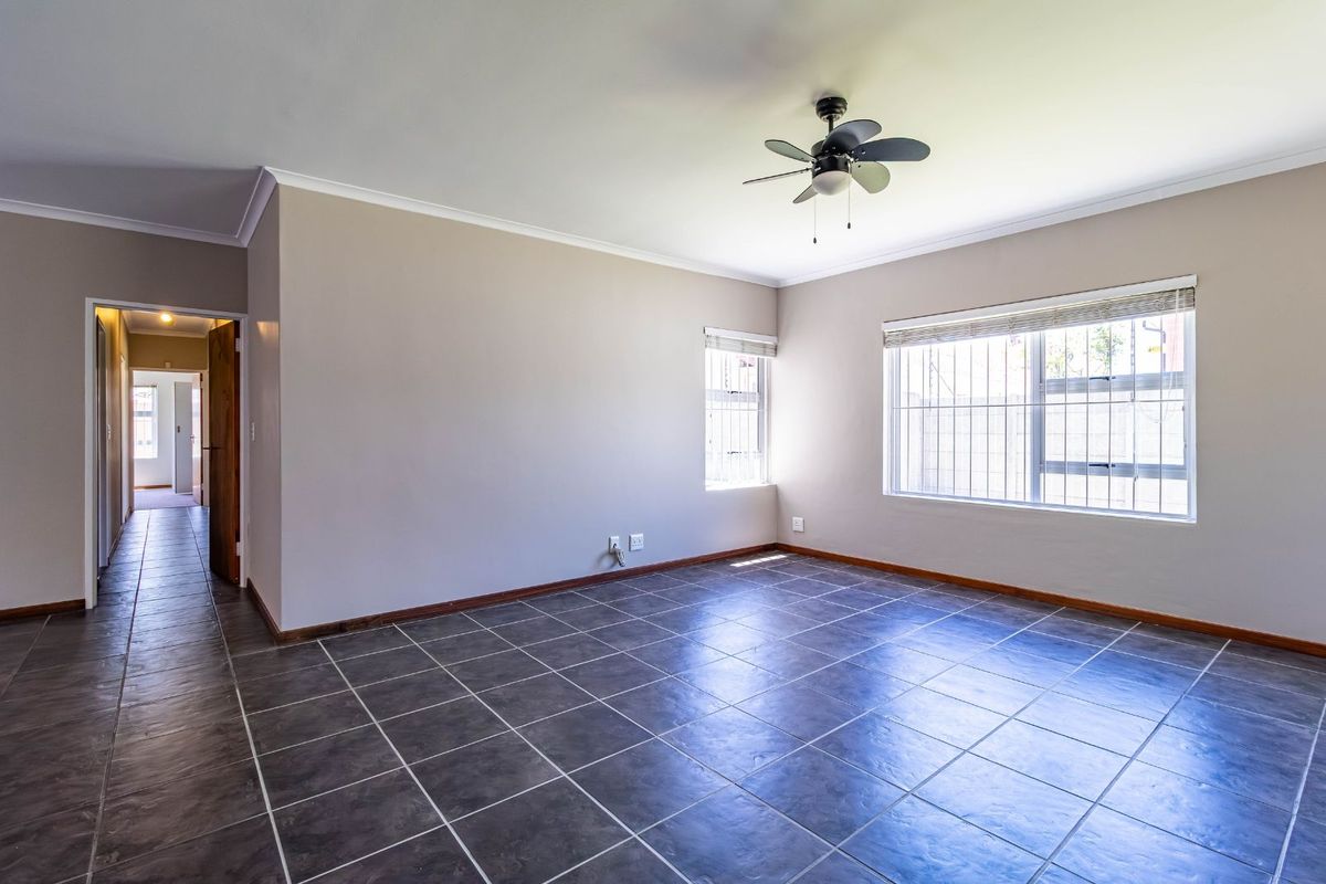A spacious, empty bedroom featuring neutral wall tones, dark tiled flooring, and a ceiling fan, offering a clean and versatile living space.