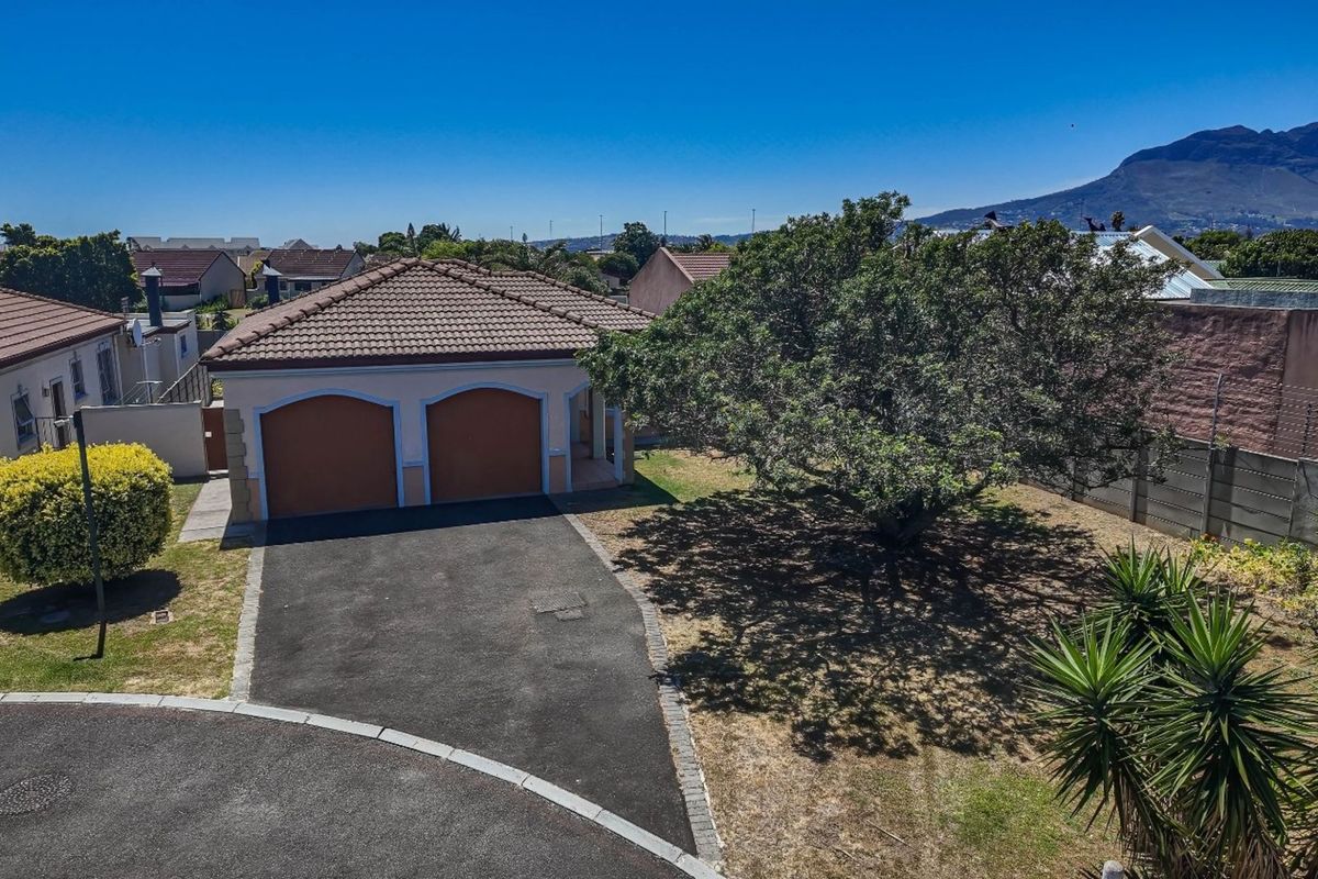 Aerial view of a residential property featuring a double garage, paved driveway, and established garden with mature trees.