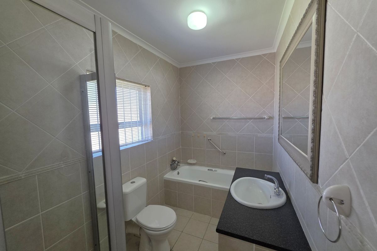 A functional bathroom featuring a built-in bathtub, separate shower enclosure, vanity with basin, and neutral wall and floor tiling.