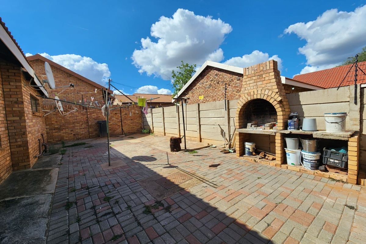 A paved rear courtyard featuring a built-in brick braai and perimeter walling, providing a functional outdoor entertainment space.
