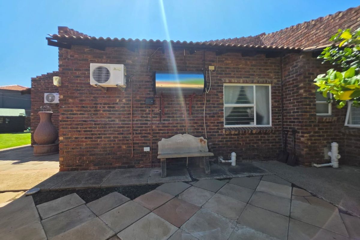 Rear exterior view of the house featuring exposed brick walls, a solar water heater, air conditioning units, and paved patio area.