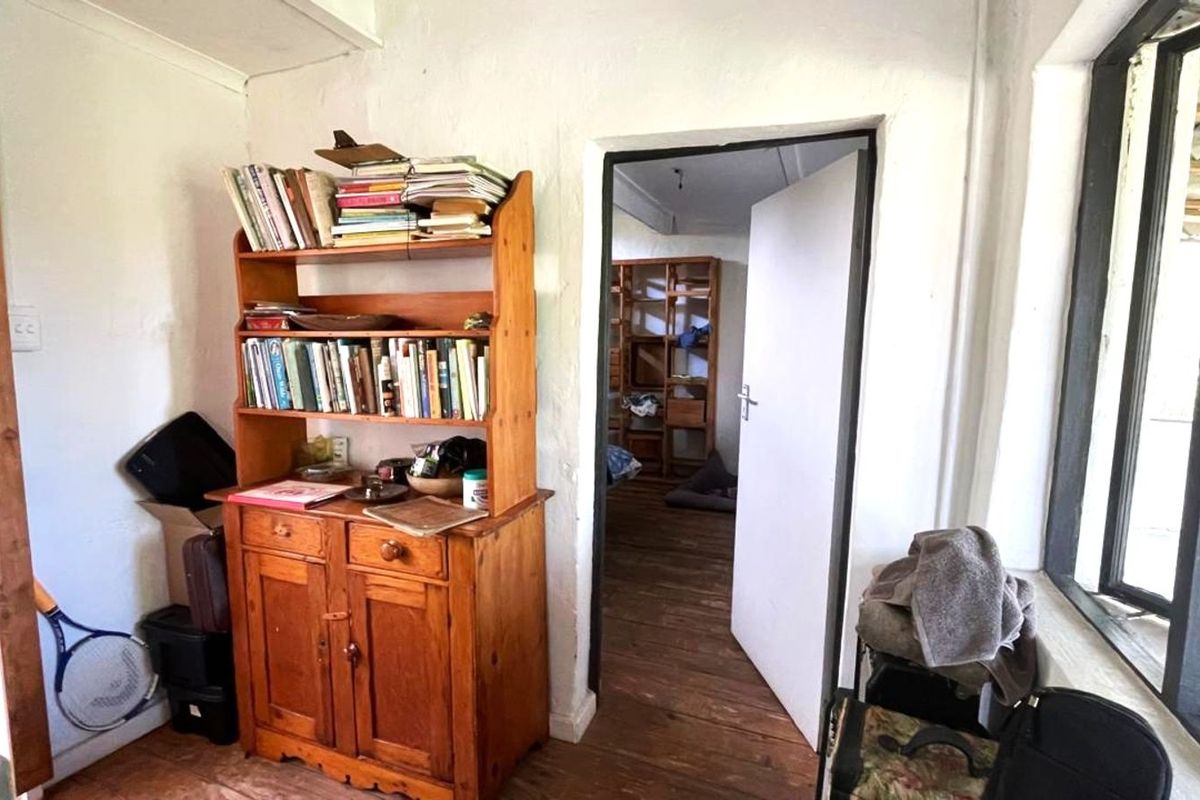 A rustic interior space featuring timber flooring, white plastered walls, and a doorway leading to an adjacent room with natural light.