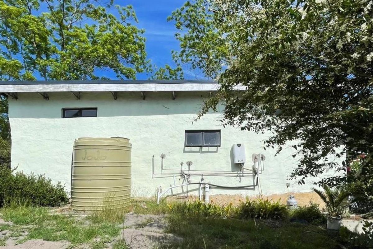 Rear exterior view of the farm building featuring a water storage tank, exposed plumbing infrastructure, and a gas water heater unit.