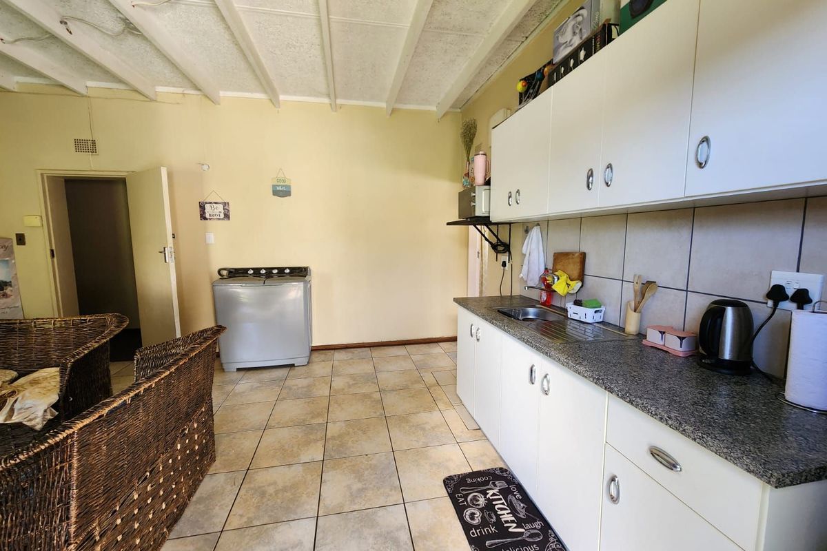 A functional kitchen area featuring white cabinetry, granite-look countertops, tiled flooring, and an exposed beam ceiling design.