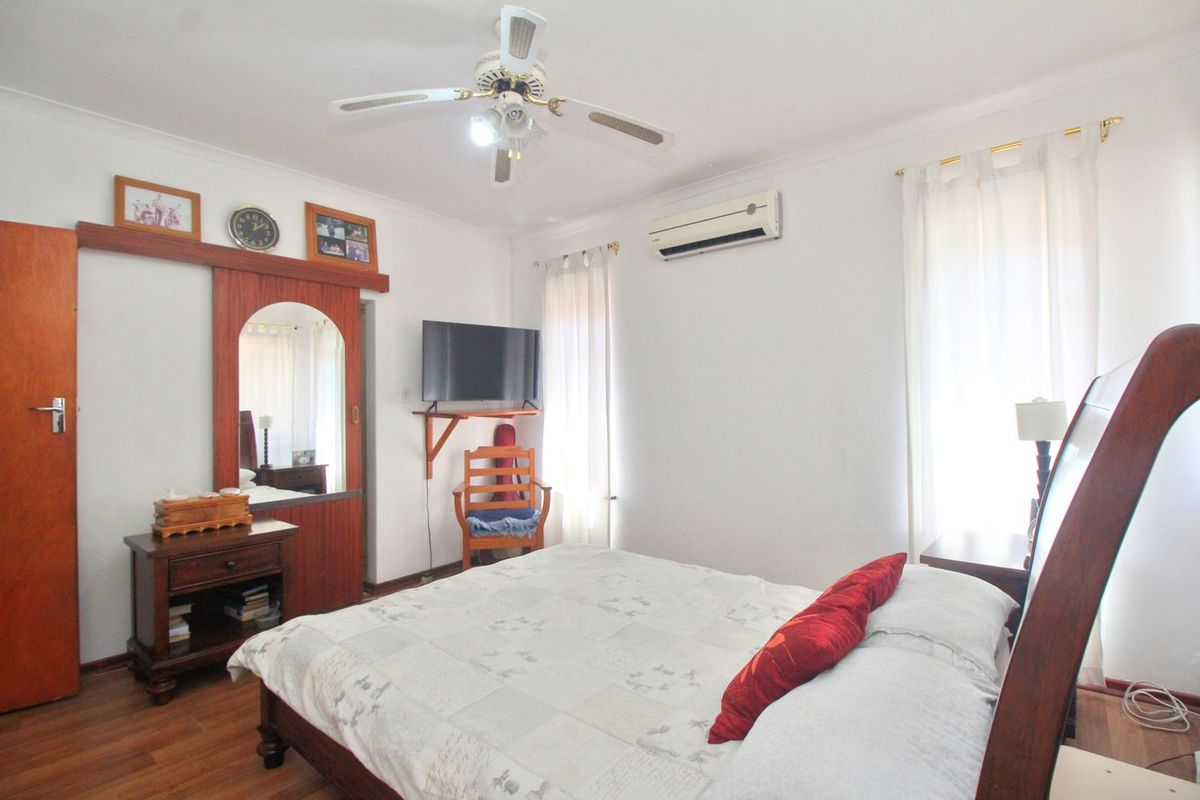 A well-lit bedroom featuring wood-look flooring, a ceiling fan, and a wall-mounted air conditioning unit.