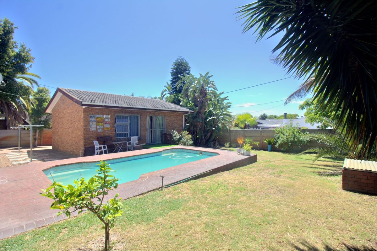 A rear garden featuring a swimming pool with brick surround, established landscaping, and a detached brick outbuilding.