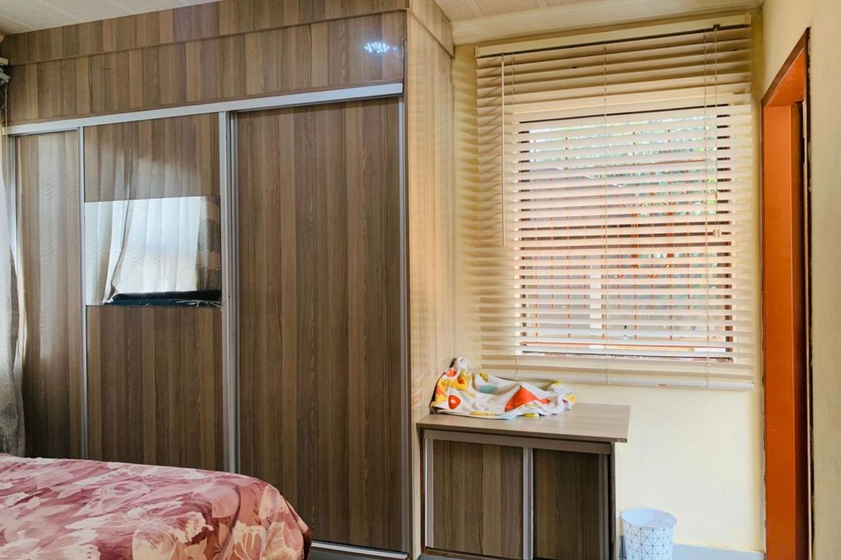 A bedroom featuring built-in wood-finish sliding door wardrobes and a matching integrated vanity or storage unit, complemented by horizontal window blinds.