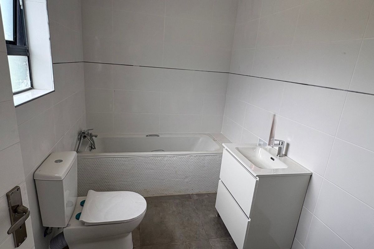 A modern bathroom featuring a white bathtub, a contemporary vanity unit with integrated basin, and a toilet, finished with neutral wall and floor tiles.
