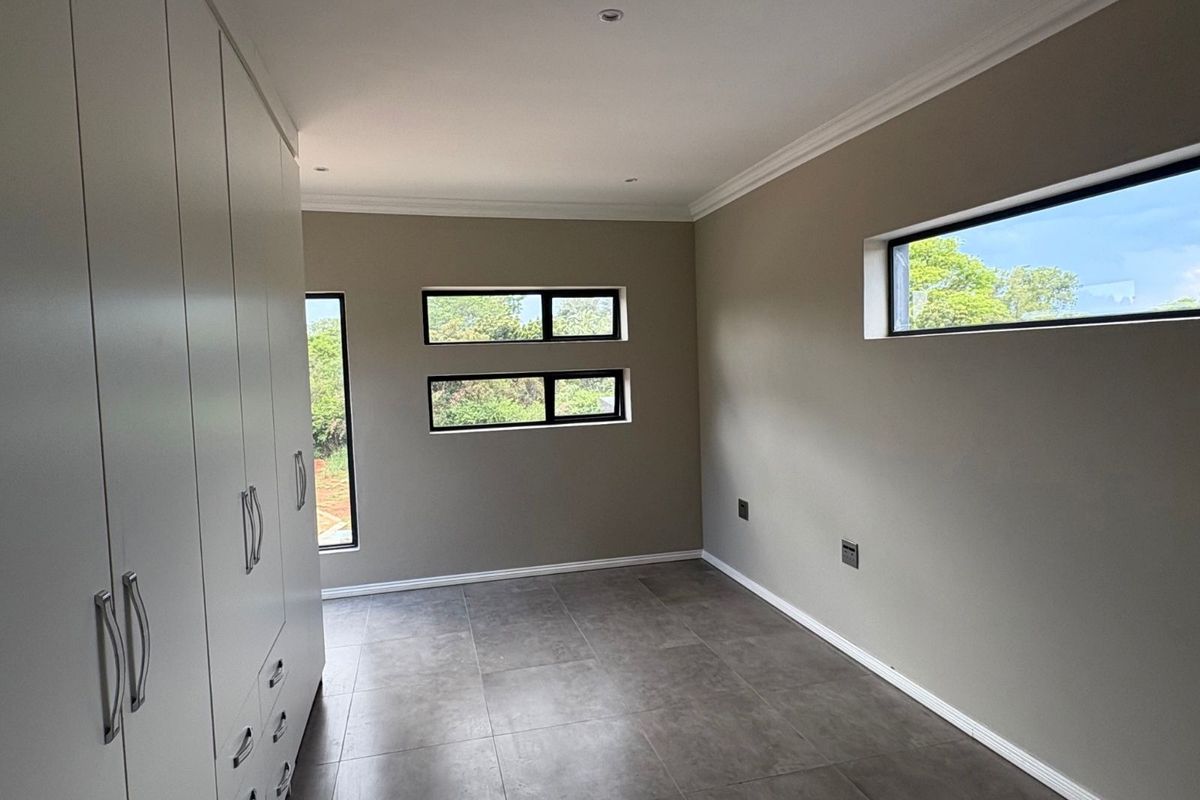 A bright, empty bedroom featuring neutral wall tones, modern grey floor tiles, and extensive built-in white cabinetry with sleek hardware.