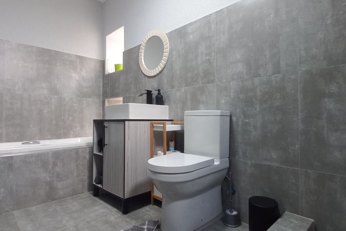 Modern bathroom featuring large-format grey wall and floor tiles, a built-in bathtub, a contemporary vanity unit with a vessel sink, and a toilet.