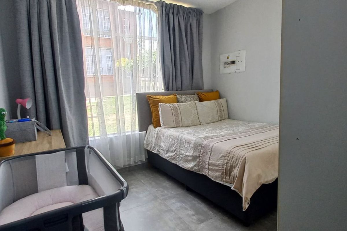 A functional bedroom featuring tiled flooring, large window with curtain tracks, and a wall-mounted electrical distribution board.