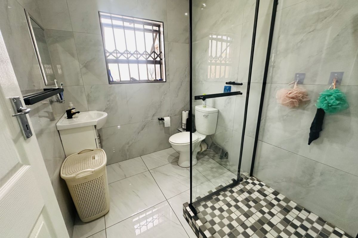 Modern bathroom featuring floor-to-ceiling marble-look wall tiles, a glass-enclosed walk-in shower with mosaic floor tiling, and a contemporary vanity basin.