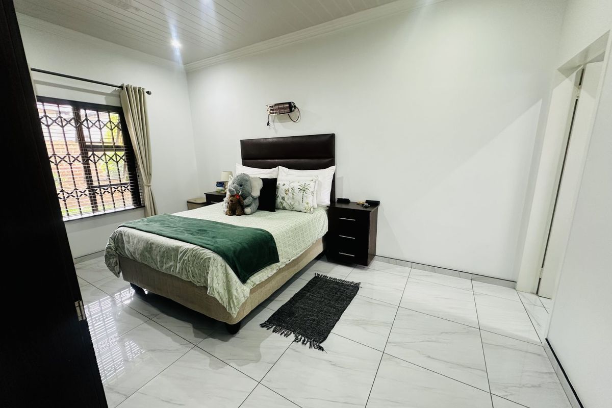 A well-maintained bedroom featuring modern white marble-look floor tiles, a tongue-and-groove ceiling, and a security-fitted window.