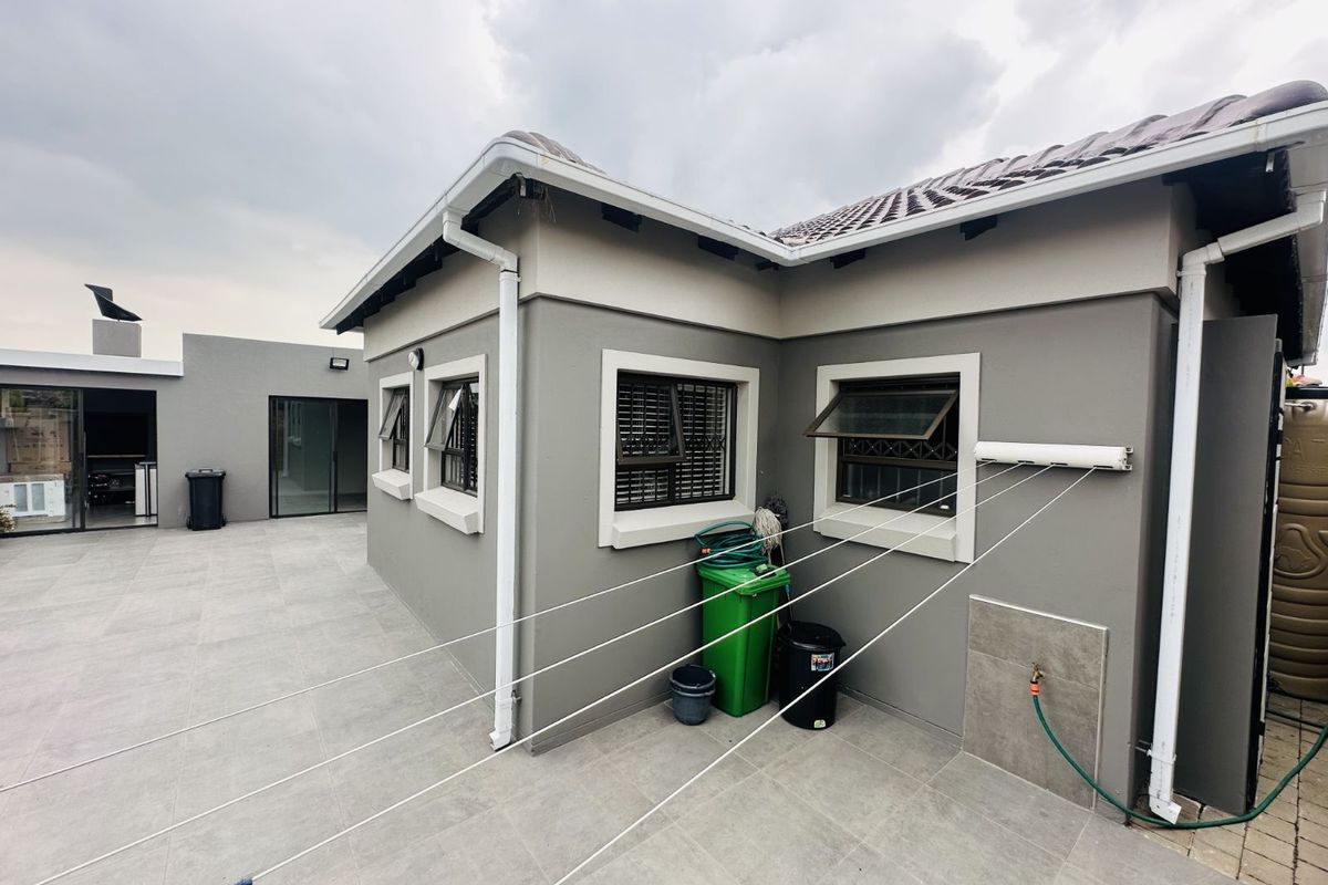 Rear exterior view of the townhouse featuring tiled patio flooring, wall-mounted retractable washing line, external water tap, and modern grey exterior wall finishes.