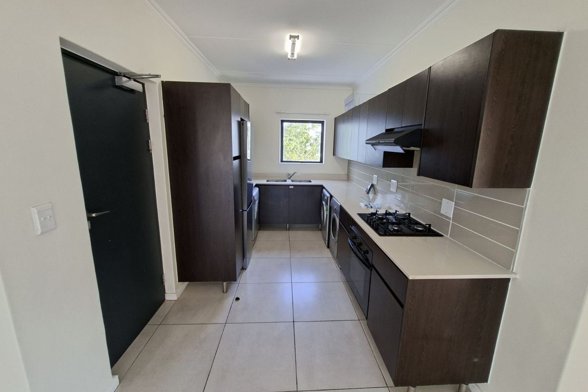 Modern galley-style kitchen featuring dark wood cabinetry, stone countertops, built-in gas hob, extractor fan, and tiled flooring.