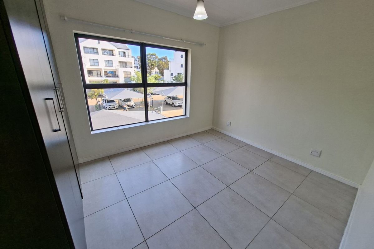 A bright, empty bedroom featuring neutral floor tiles, a large window with natural light, and a built-in wardrobe.