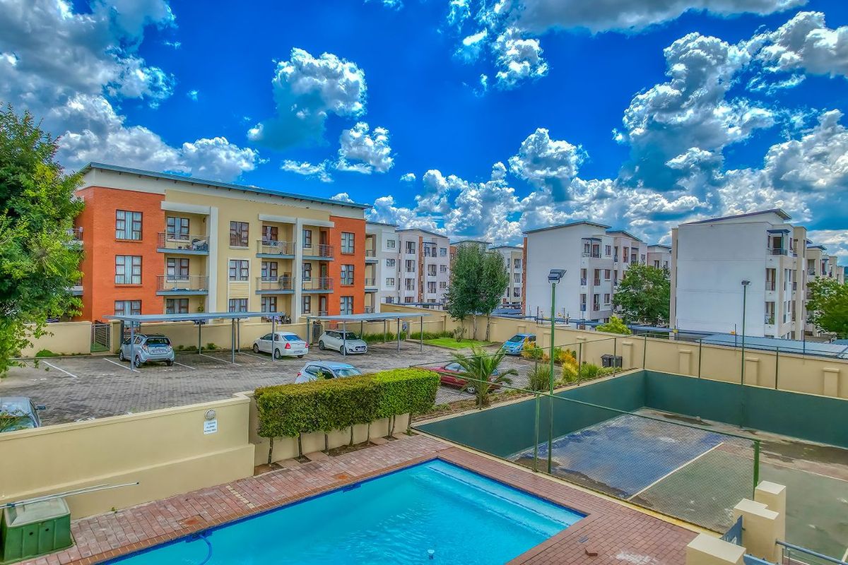 Elevated view of the apartment complex featuring a swimming pool, tennis court, and dedicated parking area with shade ports.