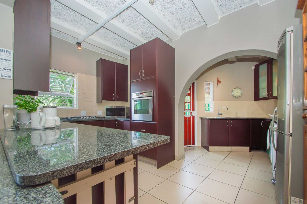 A functional kitchen featuring dark cabinetry, granite countertops, tiled flooring, and a built-in oven, connected to a secondary prep area via an arched doorway.