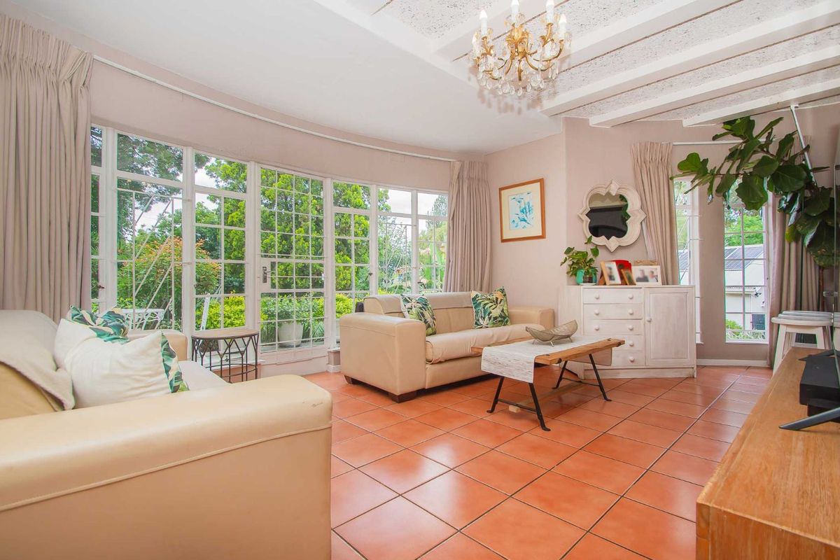 Bright living room featuring large windows with garden views, terracotta floor tiles, and exposed beam ceiling detail.
