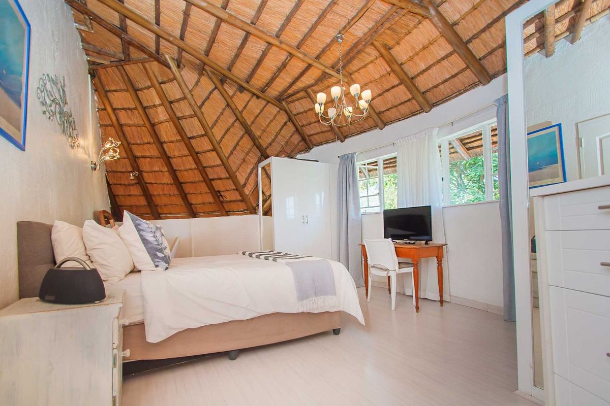 A cozy bedroom featuring a unique vaulted thatched roof, tiled flooring, and large windows that provide natural light.