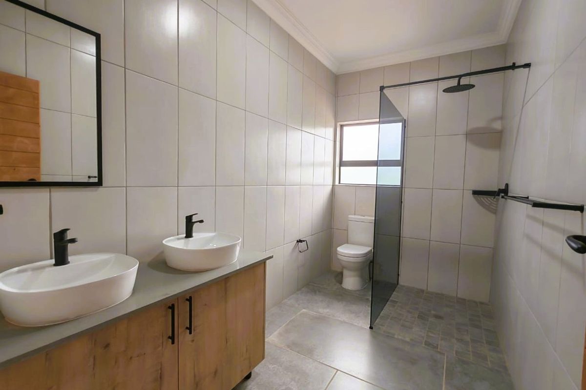 Modern bathroom featuring a double vanity with vessel sinks, a walk-in shower with a glass screen, and neutral floor-to-ceiling wall tiles.