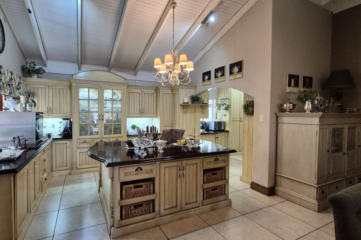 A spacious kitchen featuring a large central island with dark countertops, custom cabinetry, vaulted ceilings, and an adjoining scullery area.