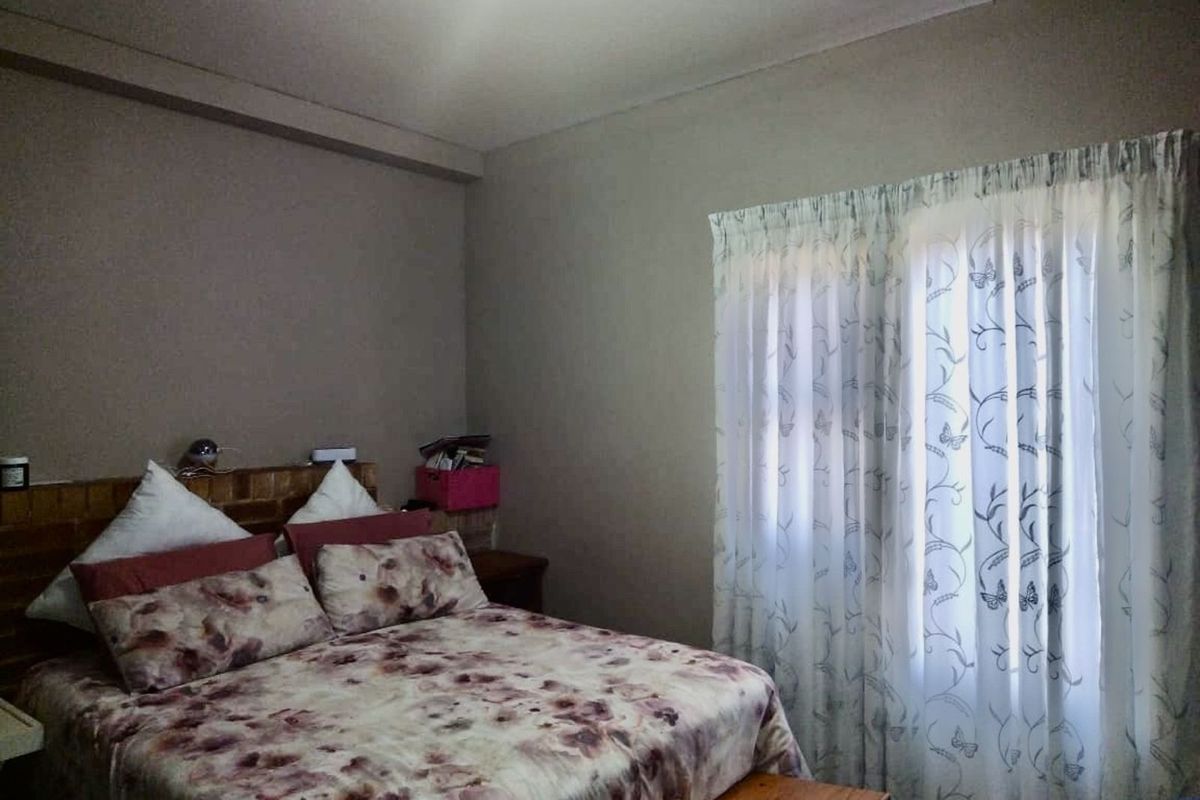A standard bedroom featuring neutral wall tones, a window with sheer curtains, and a built-in headboard structure.