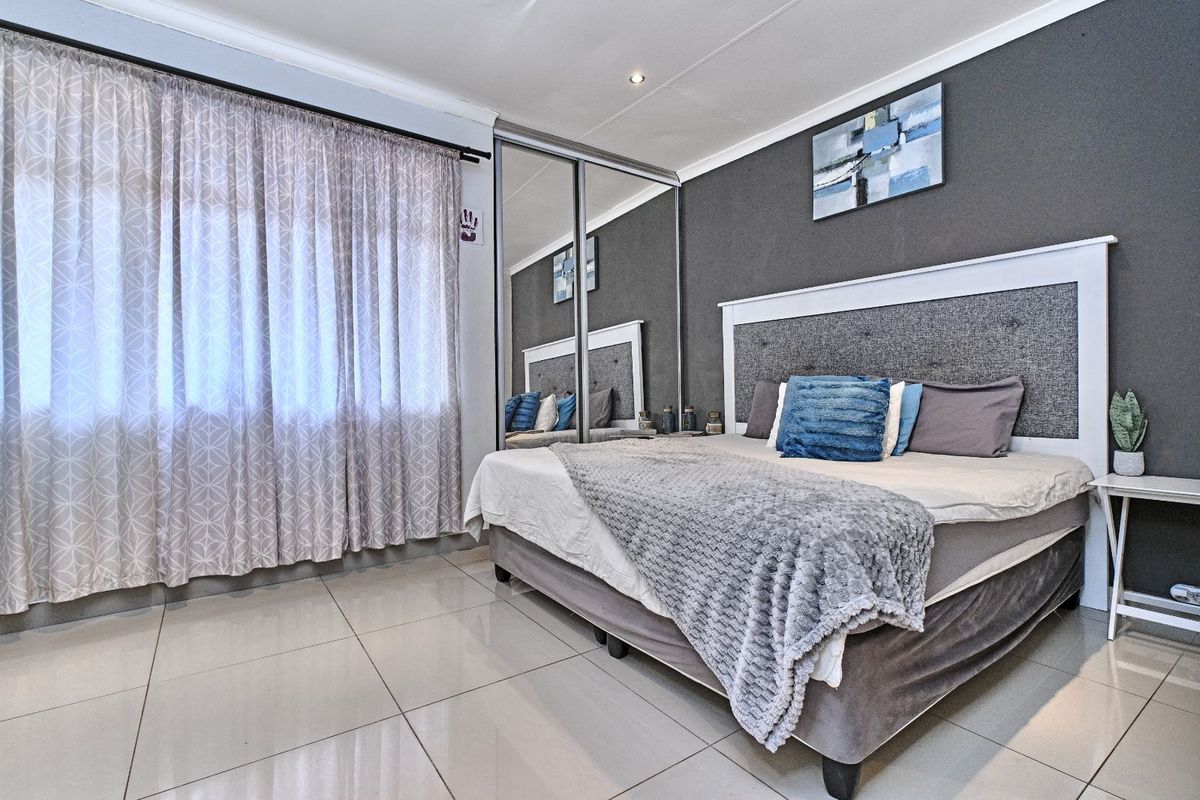 A well-maintained bedroom featuring large format floor tiles, built-in mirrored sliding door cupboards, and recessed ceiling lighting.